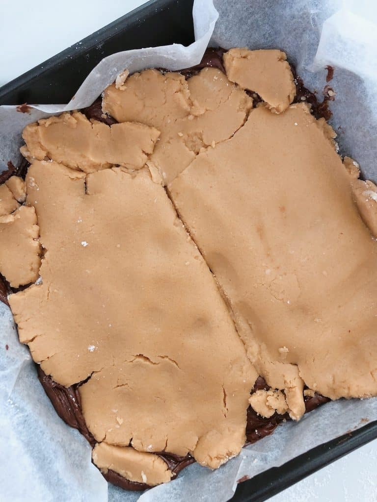 brownie mixture layered of peanut butter on top on a baking tin