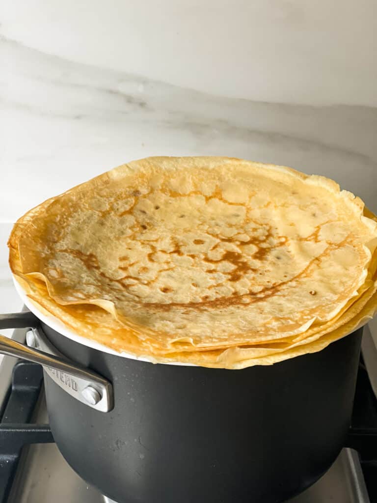 Thermomix crepes stacked on a saucepan to keep warm