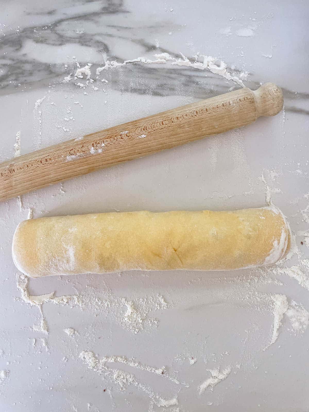 Cinnamon roll dough rolled into sausage shape with rolling pin alongside.