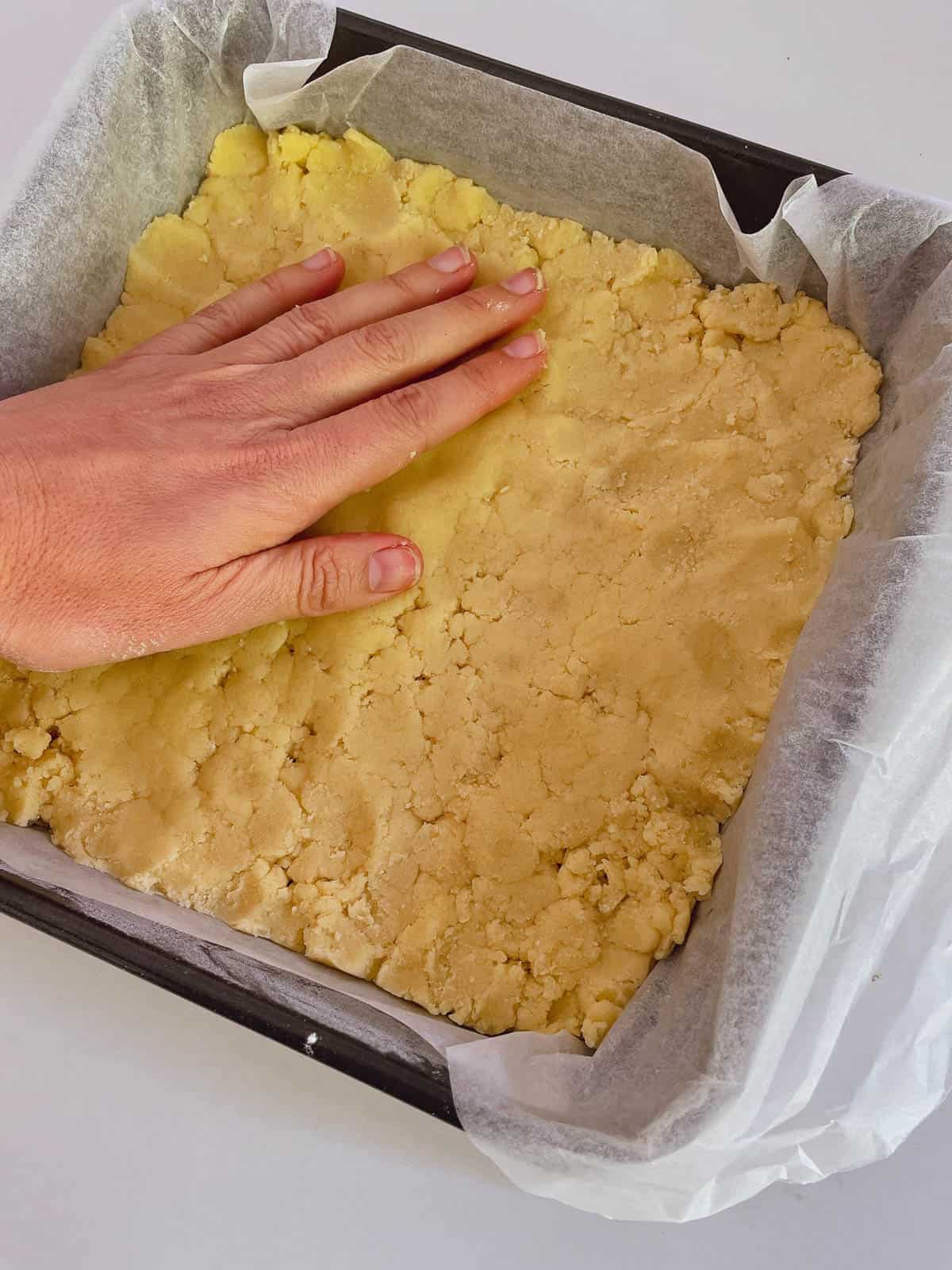 Pressing shortbread crumbs into cake tin.