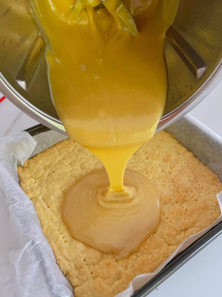 Pouring caramel sauce from Thermomix jug onto shortbread base.