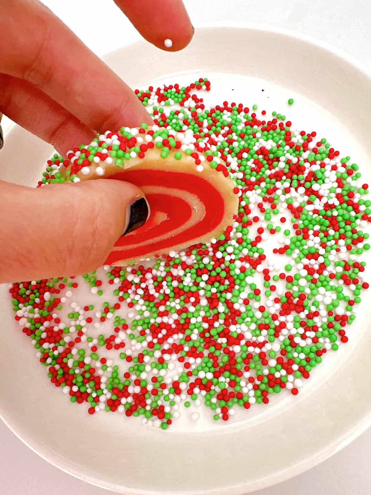 Rolling pinwheel cookie in sprinkles. 