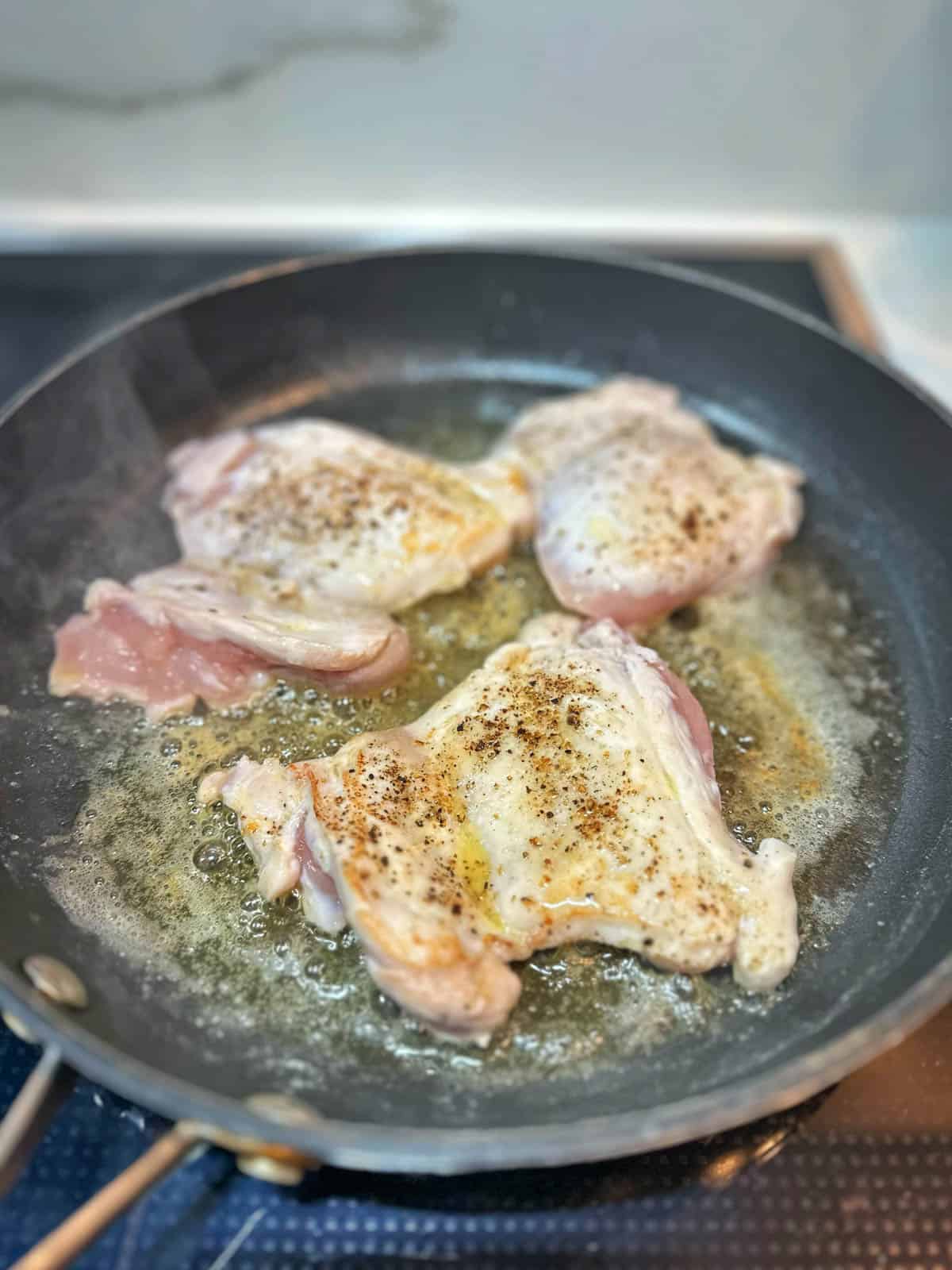 Searing chicken thigh fillets in a frying pan. 