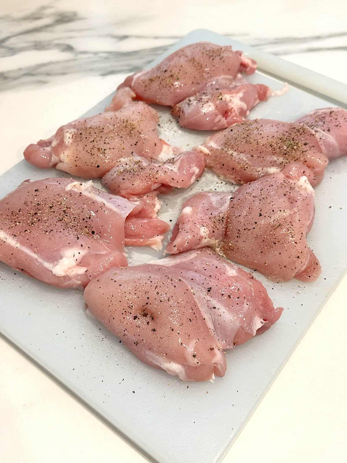 Seasoned chicken thigh fillets on a chopping board. 