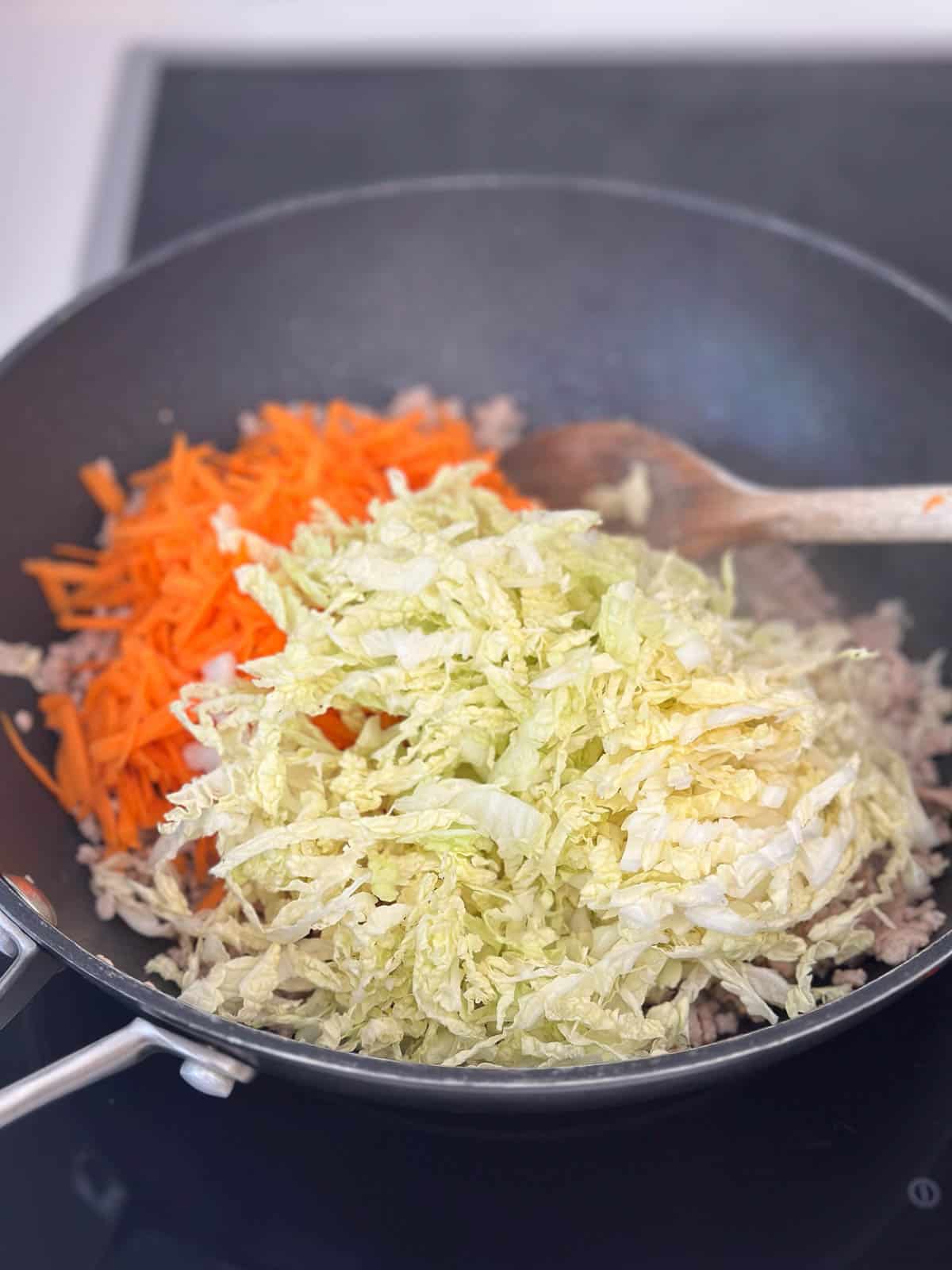 Adding carrot and cabbage to wok.