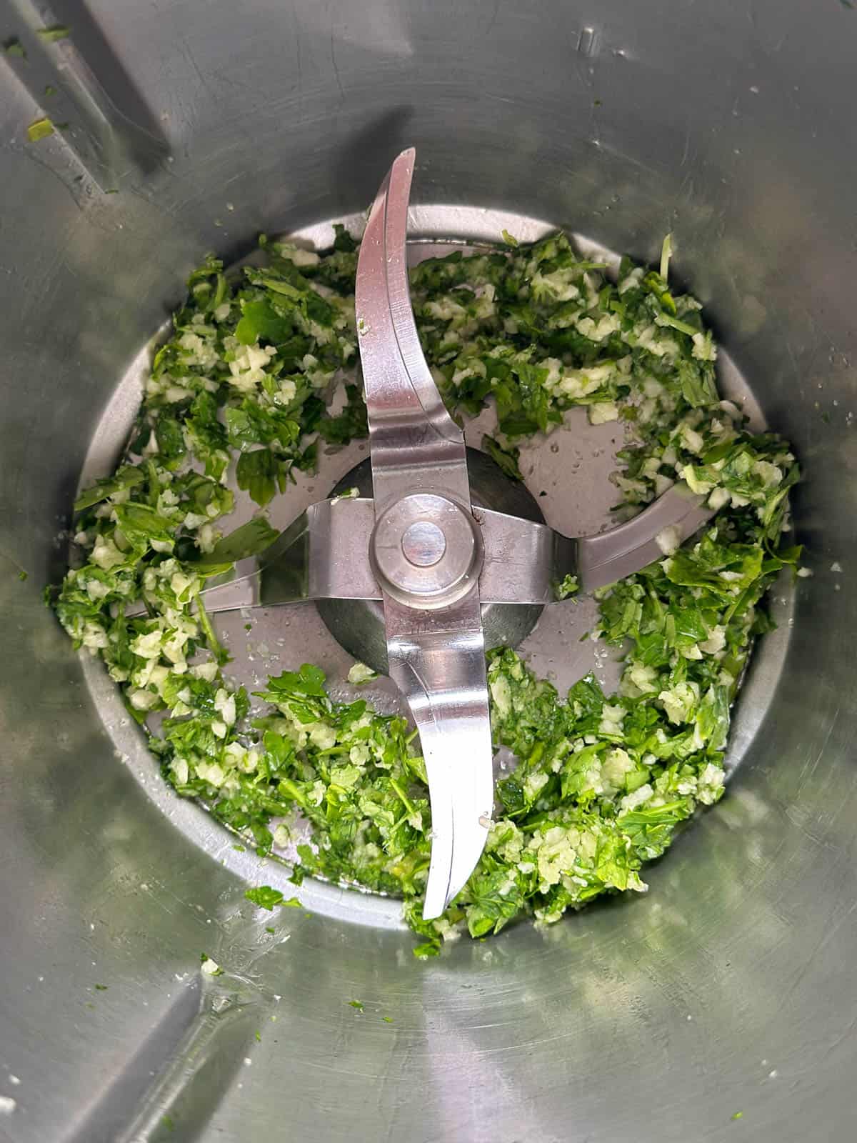 Chopped garlic and parsley in a Thermomix bowl.