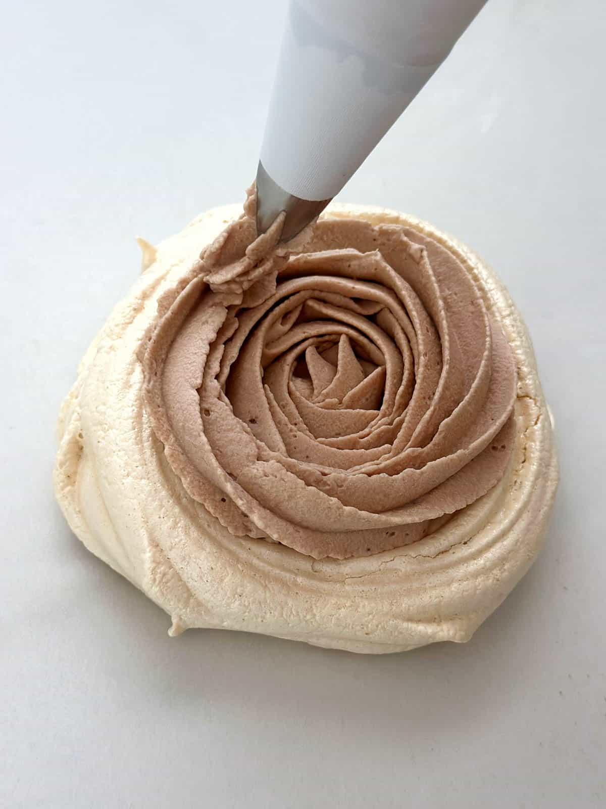 Piping chocolate whipped cream onto a meringue nest.
