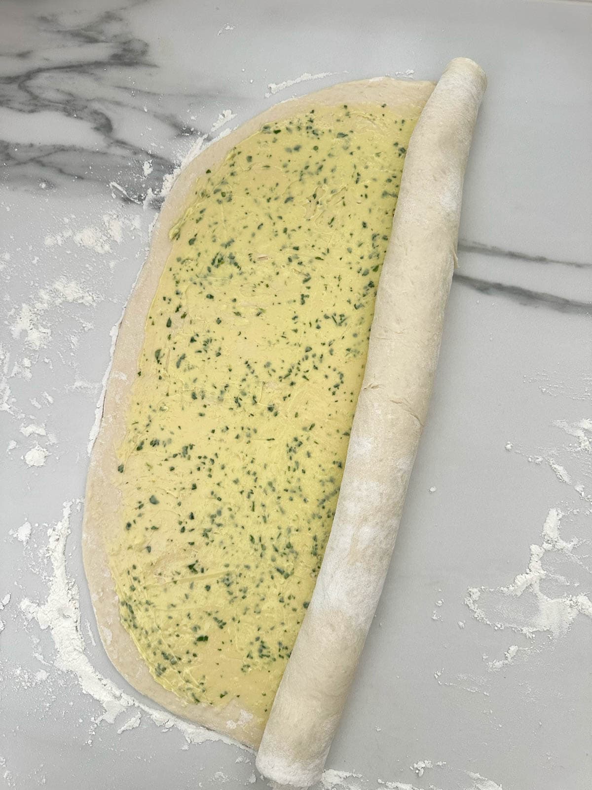 Rolling the garlic bread dough into a large scroll shape.