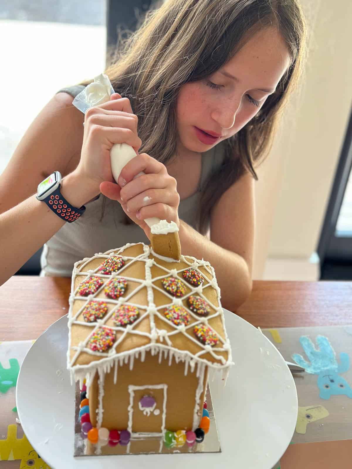 Girl icing gingerbread house with Thermomix Royal Icing.