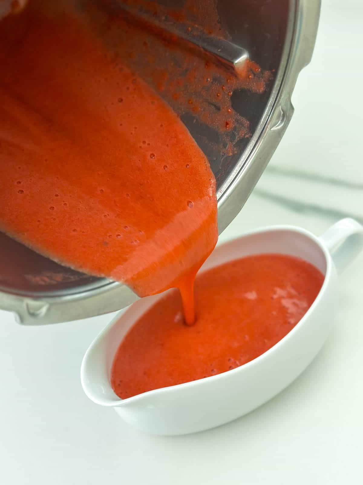 Pouring strawberry sauce from Thermomix bowl into serving jug. 