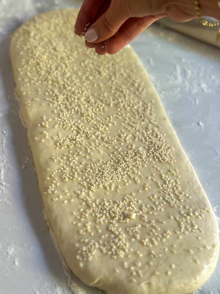 Sprinkling sesame seeds over dough for homemade Thermomix Grissini.