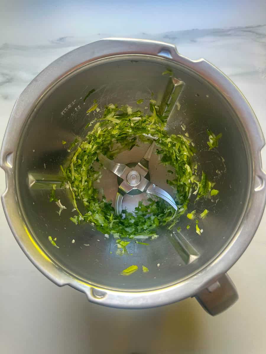 Chopped spring onions and parsley in a Thermomix bowl.