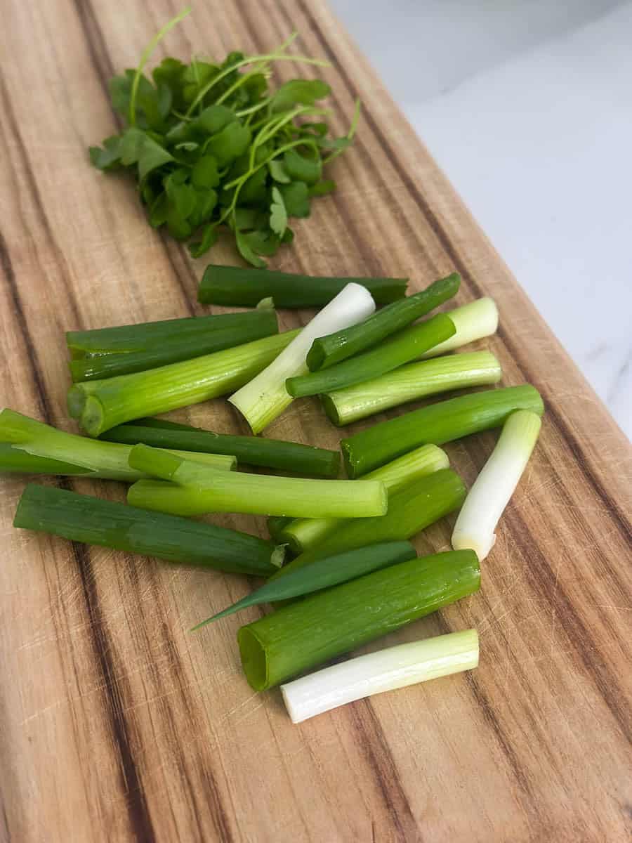 Chopped spring onions and parsley leaves on a chopping board.