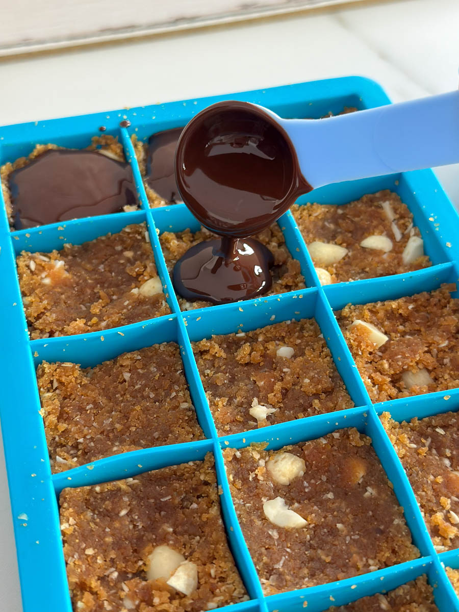 Pouring chocolate over Thermomix Peanut Butter Chocolate Energy Bites in an ice tray.