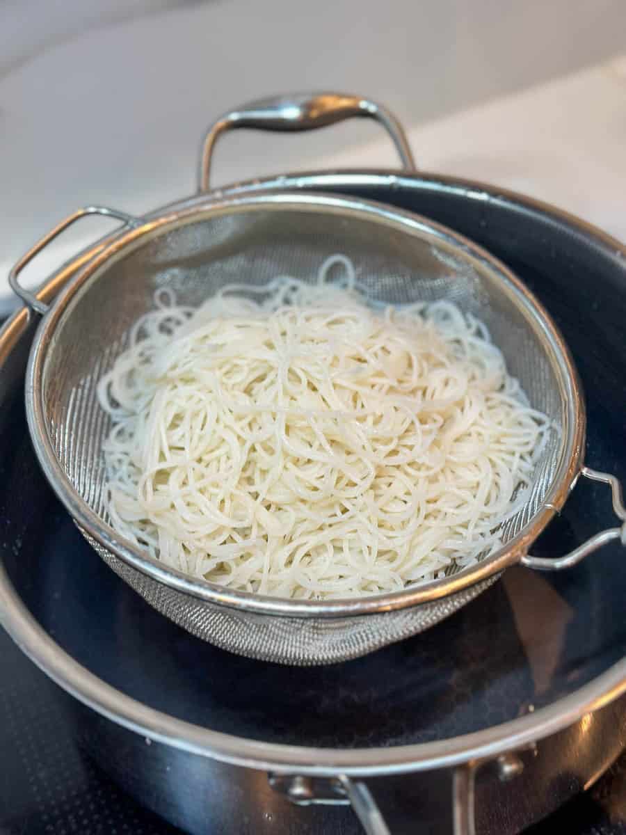 Draining cooked rice noodles in a sieve.