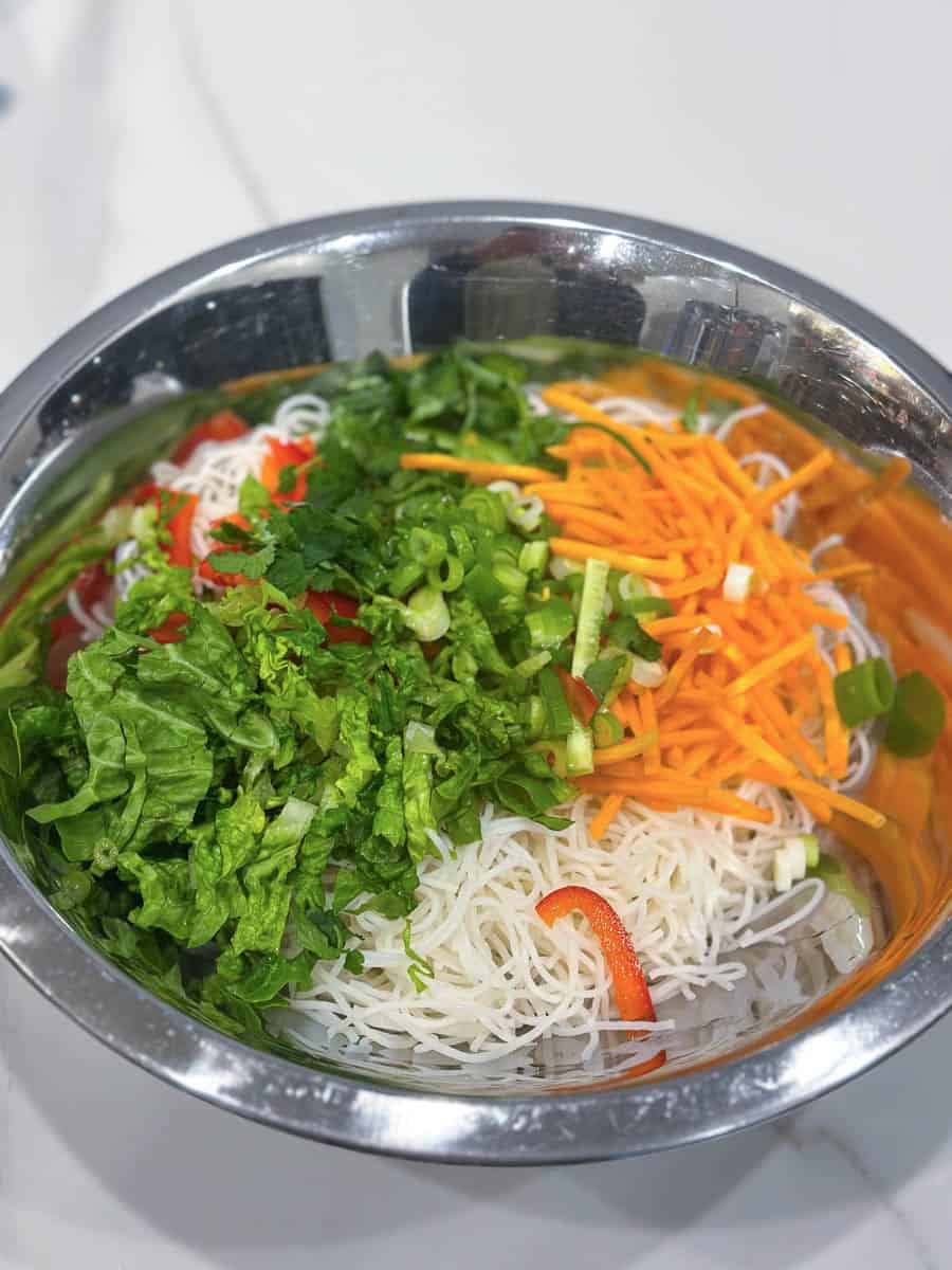 Rice noodles and chopped vegetables in a bowl.